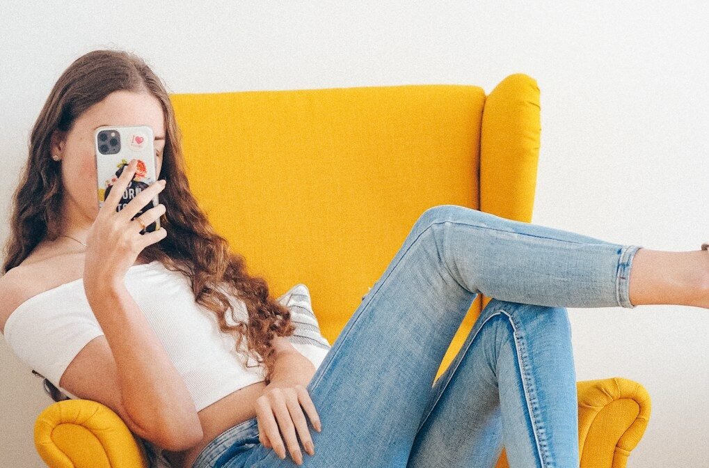 woman in white tank top and blue denim jeans sitting on yellow sofa